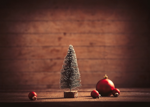 Kleiner Weihnachtsbaum und Kugeln auf Holztisch und Hintergrund