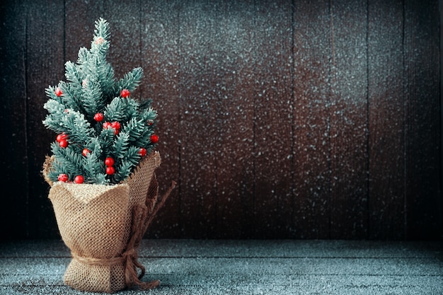 Kleiner Weihnachtsbaum verpackte in der Leinwand auf dunklem schneebedecktem Hintergrund