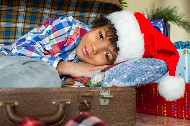 Kleiner Weihnachtsmann, der neben Geschenken legt. Kind im Koffer in der Nähe von Geschenken. Überraschung ist so nah. Im Urlaub werden Träume wahr.