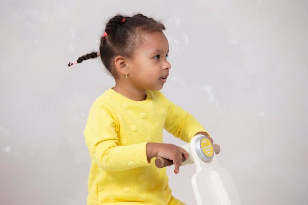 Kleines afroamerikanisches Mädchen in einem gelben Kleid mit lockigen Zöpfen auf hellem Hintergrund.