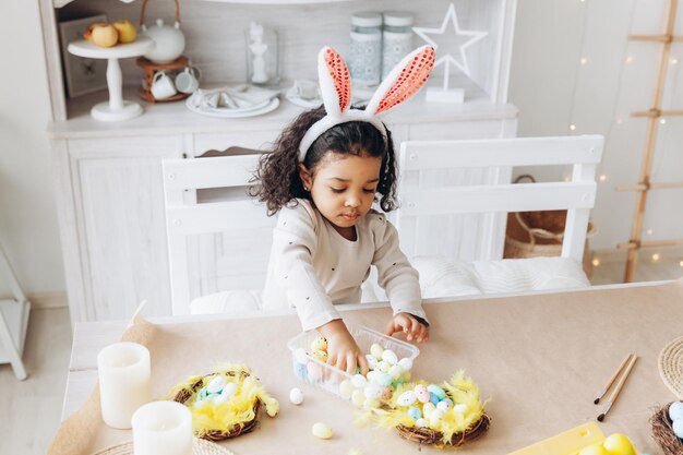 Kleines afroamerikanisches Mädchen malt Ostereier zu Hause in der Küche fröhliche ostern