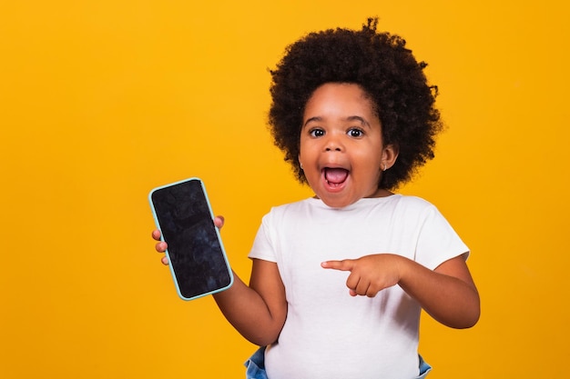 Kleines afrokindmädchen, das ein telefon hält und lokalisiert auf gelbem hintergrund zeigt.