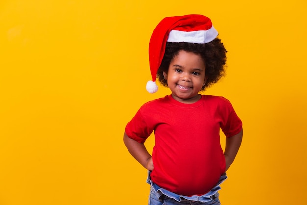 Kleines Afromädchen in rotem T-Shirt und Weihnachtsmütze gekleidet für Weihnachten. Weihnachts- und Neujahrsaktion