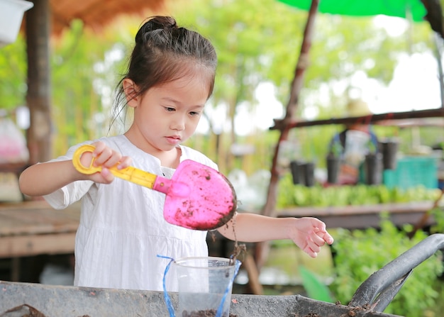 Kleines asiatisches Kindermädchen, das den Baum im Topf pflanzt.