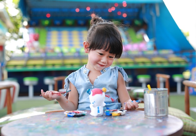 Kleines asiatisches Kindermädchen des Porträts, das Spaß hat, auf Stuckpuppe zu malen