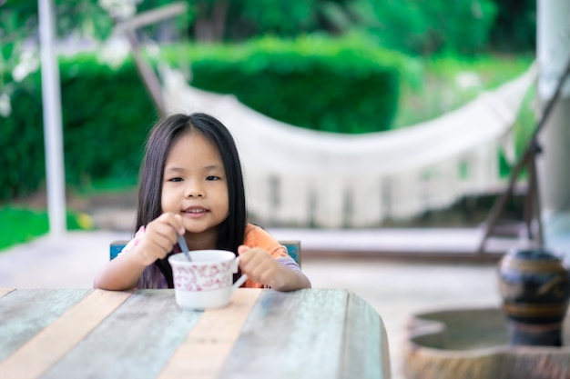 Kleines asiatisches Mädchen bereiten heißen Kakao oder Schokolade zum Trinken zu, um Frühstück am Morgen zu genießen