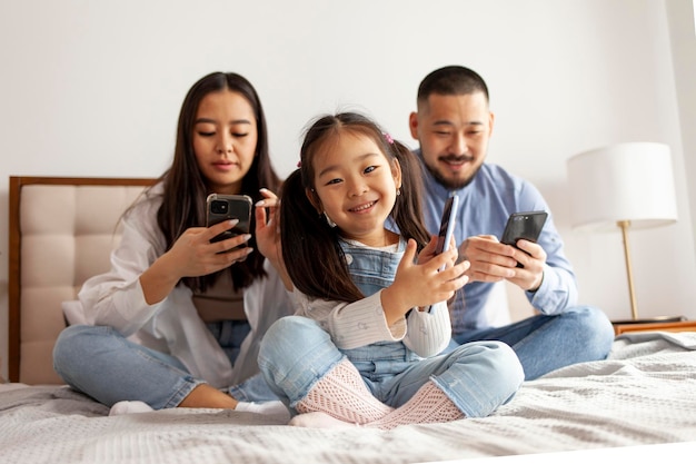 Kleines asiatisches Mädchen mit Mama und Papa nutzen Smartphone, koreanische glückliche junge Familie mit mobilen Geräten