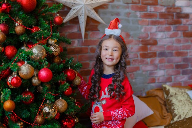 Kleines asiatisches Mädchen schmückt Weihnachtsbaum lächelnd Weihnachten, neues Jahr