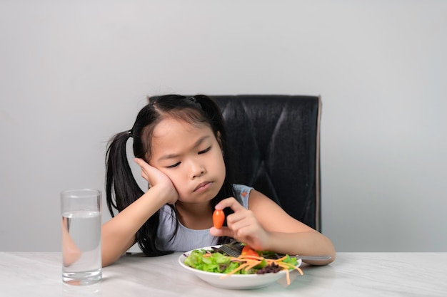 Kleines asiatisches süßes Mädchen weigert sich, gesundes Gemüse zu essenErnährungskonzept für gesunde Ernährung für KinderKinder essen kein Gemüse gern