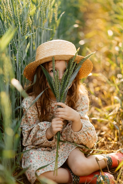 Kleines attraktives Mädchen mit Strohhut läuft auf einem Weizenfeld mit grünen Ohren