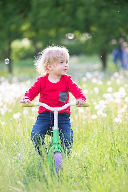 Kleines Baby auf einem Fahrrad auf einer grünen Wiese