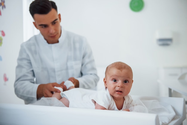 Kleines Baby, das auf dem Tisch liegt. Der junge Kinderarzt ist tagsüber in der Klinik.