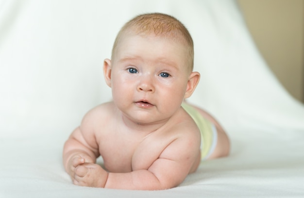 Kleines Baby, das auf der weißen Decke liegt und sich freut