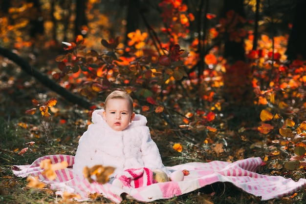 Kleines Baby, das auf einer Decke im Herbstwald sitzt