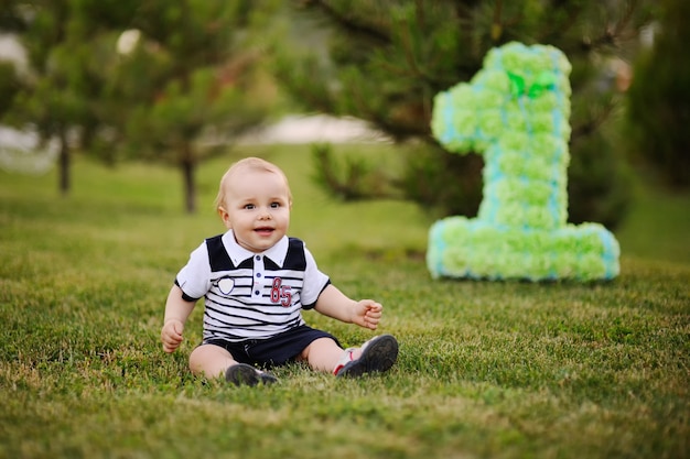 Kleines Baby, das auf Gras sitzt und an seinem ersten Geburtstag lächelt