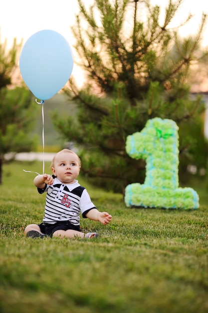 Kleines Baby, das auf Gras sitzt und an seinem ersten Geburtstag lächelt