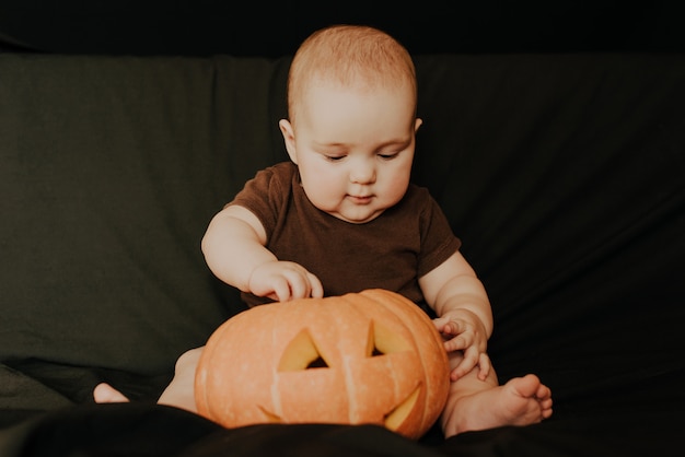 Kleines Baby, das mit Halloween-Kürbis Jack sitzt