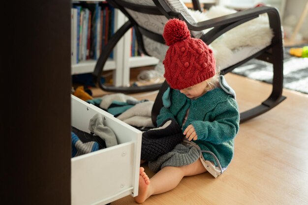 Foto kleines baby, das sich zu hause einen warmen hut und schal anprobiert, kleines kind, das mit warmen winterhüten spielt