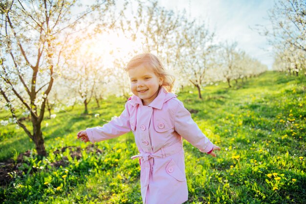 Kleines Baby, das zwischen blühenden Bäumen bei Sonnenuntergang läuft. Ar