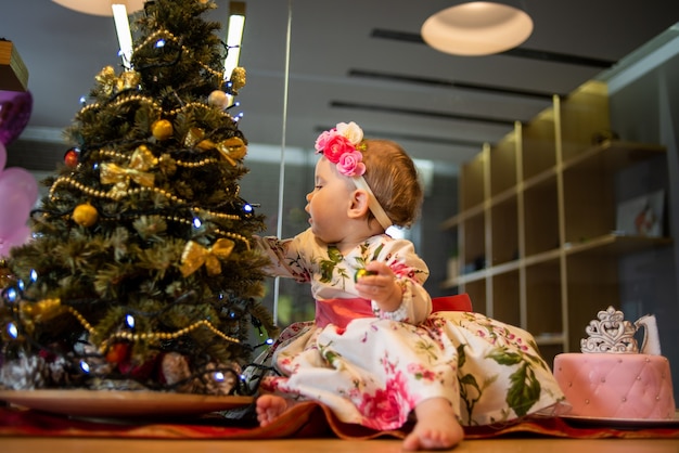 Kleines Baby in der Nähe von Weihnachtsbaum vor der Neujahrsparty