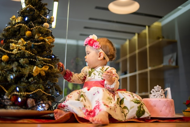 Kleines Baby in der Nähe von Weihnachtsbaum vor der Neujahrsparty