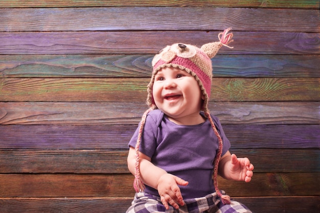 Kleines Baby in einem lustigen Eulenhäkelhut über blauer Holzwand