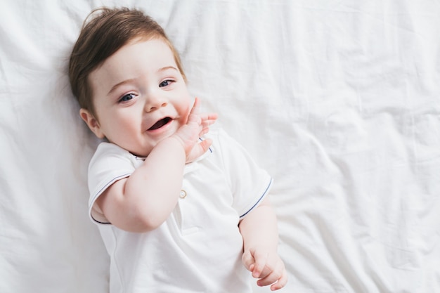 Kleines Baby lacht glücklich auf einem Bett mit einem weißen Laken