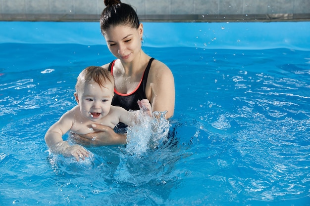 Kleines Baby lernt mit dem Lehrer im Pool zu schwimmen