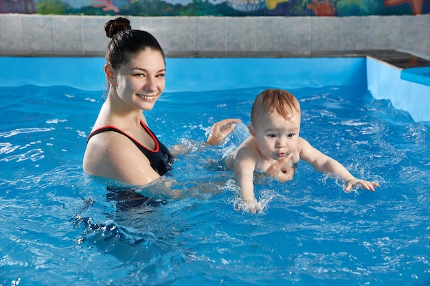 Foto kleines baby lernt mit dem lehrer im pool zu schwimmen