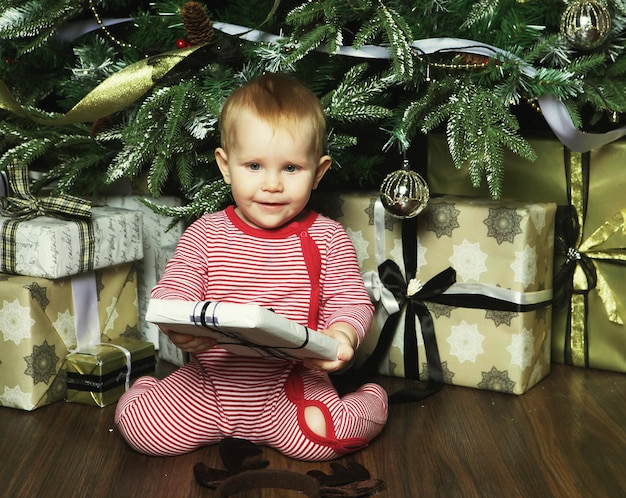 Kleines Baby mit der Geschenkkiste in der Nähe des Weihnachtsbaums