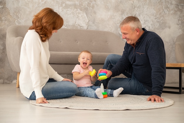 Kleines Baby sammelt eine Pyramide mit Großeltern am Wohnzimmer. Familie verbringen Zeit miteinander drinnen, livestile