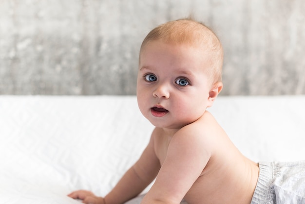 kleines Baby von neun Monaten liegt auf dem Bauch und stützt sich auf seine Hände. Kind lernt krabbeln Auf dem Bett zu liegen ist ein Kopierraum