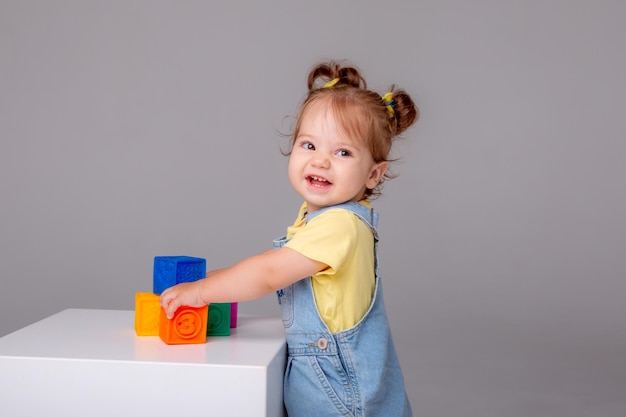 kleines Babymädchen sitzt auf weißem Hintergrund und spielt mit bunten Würfeln