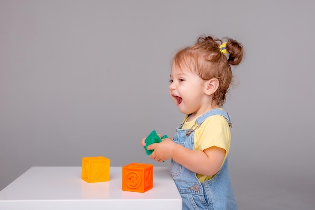 kleines Babymädchen sitzt auf weißem Hintergrund und spielt mit bunten Würfeln