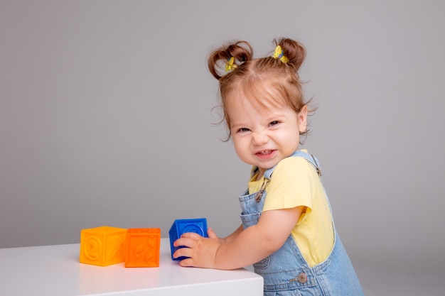 kleines Babymädchen sitzt auf weißem Hintergrund und spielt mit bunten Würfeln