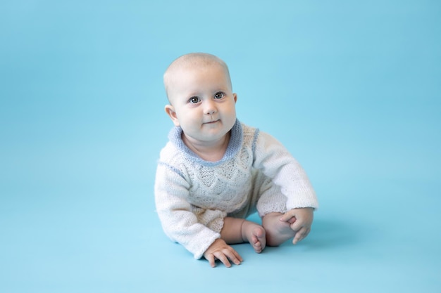 Kleines blondes Baby in einem Strickpullover auf blauem Hintergrund isolieren, Platz für Text, Baby Kleinkind in Winterkleidung, Winter