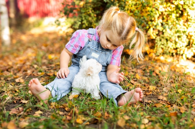 Kleines blondes Kleinkindmädchen mit zwei Borten, die mit nettem weißem Welpen spielen