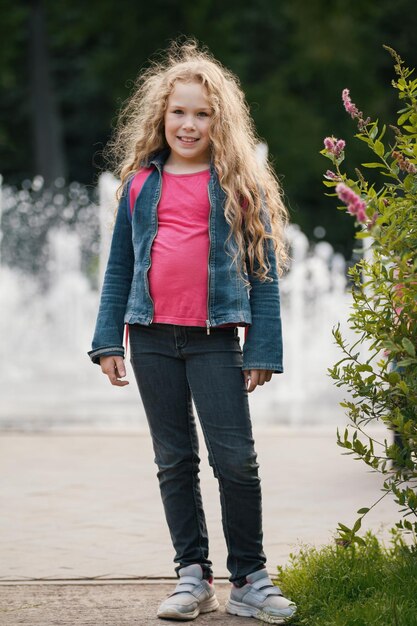 Kleines blondes lächelndes Kind, das Jeansjacke im Park trägt, Porträt im Freien