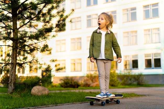 Kleines blondes Mädchen auf einem Skateboard in der Stadt
