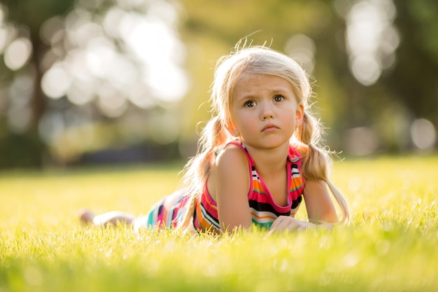 kleines blondes Mädchen, das auf dem Lächeln des grünen Grases liegt