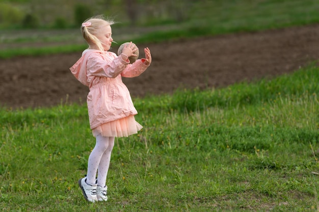 Kleines blondes Mädchen im rosa Outfit fängt Ball auf der Wiese Rückansicht Kind spielt draußen mit dem Ball