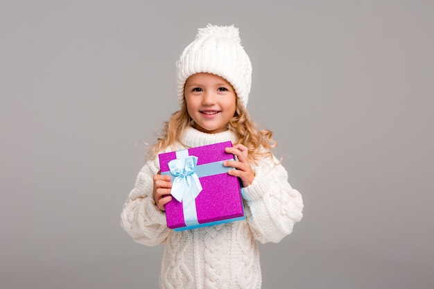 Kleines blondes Mädchen im Winterhut lächelnd, eine Geschenkbox halten