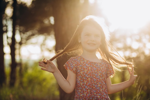 Kleines blondes Mädchen in beigem Musselinkleid hält Weizenkörner in der Handfläche im Weizenfeld bei Sonnenuntergang