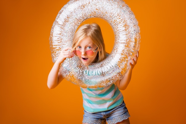 Kleines blondes Mädchen in der Sonnenbrille hält einen Schwimmkreis in ihren Händen und lächelt