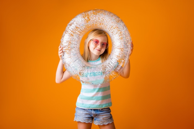 Kleines blondes Mädchen in der Sonnenbrille hält einen Schwimmkreis in ihren Händen