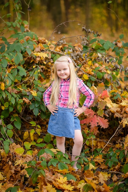 Kleines blondes Mädchen in einem Hemd und in Jeansshorts geht in den Herbstpark.