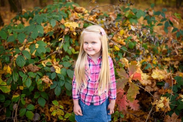 Kleines blondes Mädchen in einem Hemd und in Jeansshorts geht in den Herbstpark.