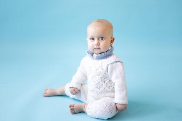 Kleines blondes Mädchen in einem Strickpullover auf blauem Hintergrund isoliert Platz für Text Baby Kleinkind in Winterkleidung Winter