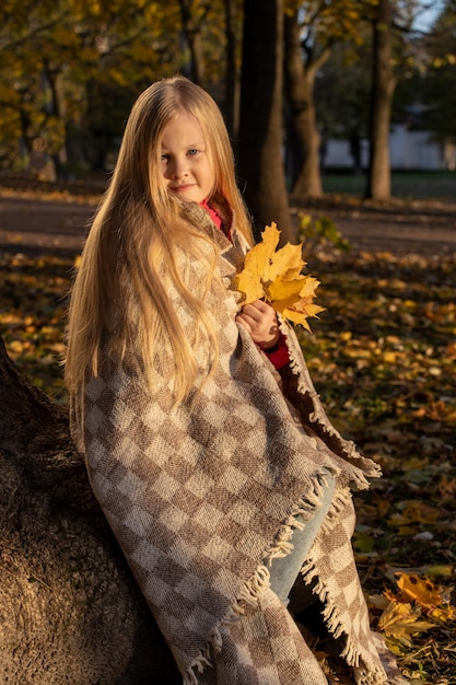 Kleines blondes Mädchen in einer karierten Peitsche im Park im Herbst