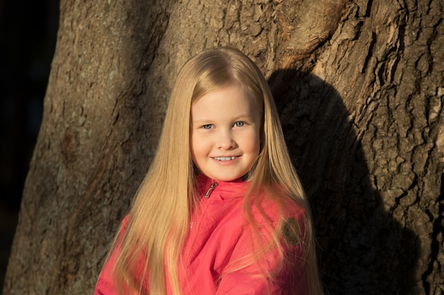 Kleines blondes Mädchen in einer rosa Jacke im Park im Herbst